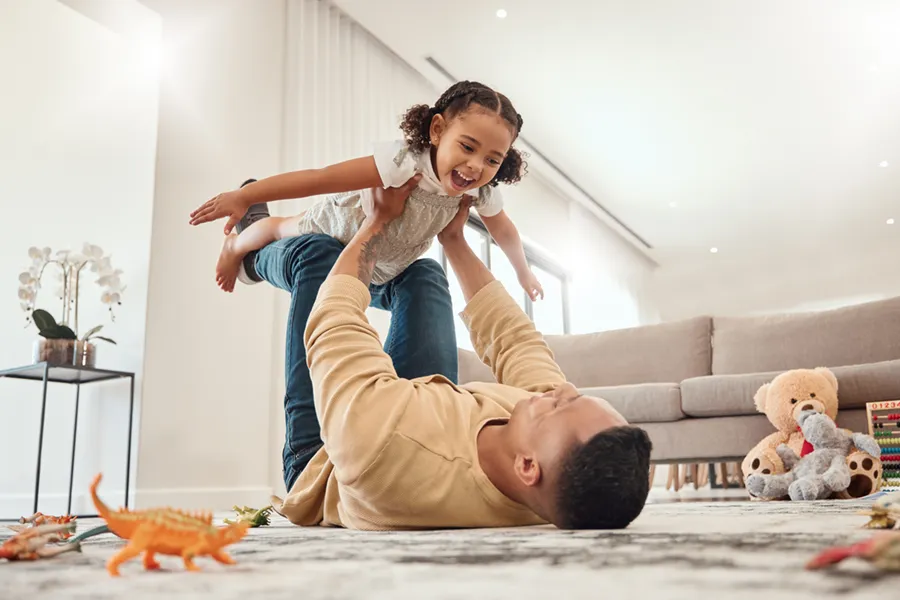 A father playing airplane with his young daughter in their climate controlled living room.