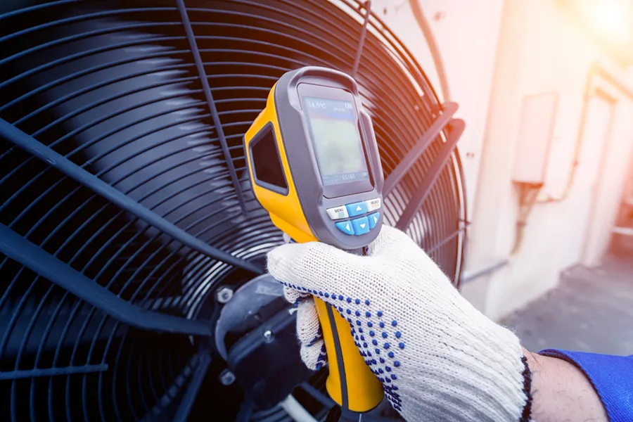 An HVAC technician checking the temperature of an air conditioner fan with a visual thermometer.