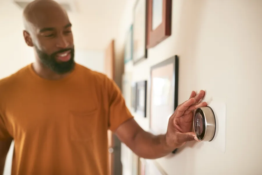 A middle-aged African-American man adjusting the smart thermostat inside his home.