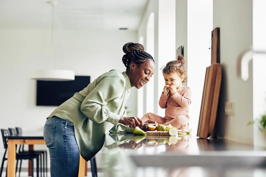 A mother and her young child in the kitchen snacking on pears.