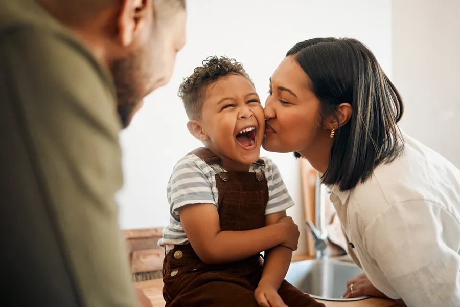 A mother kissing her laughing toddler's cheek.