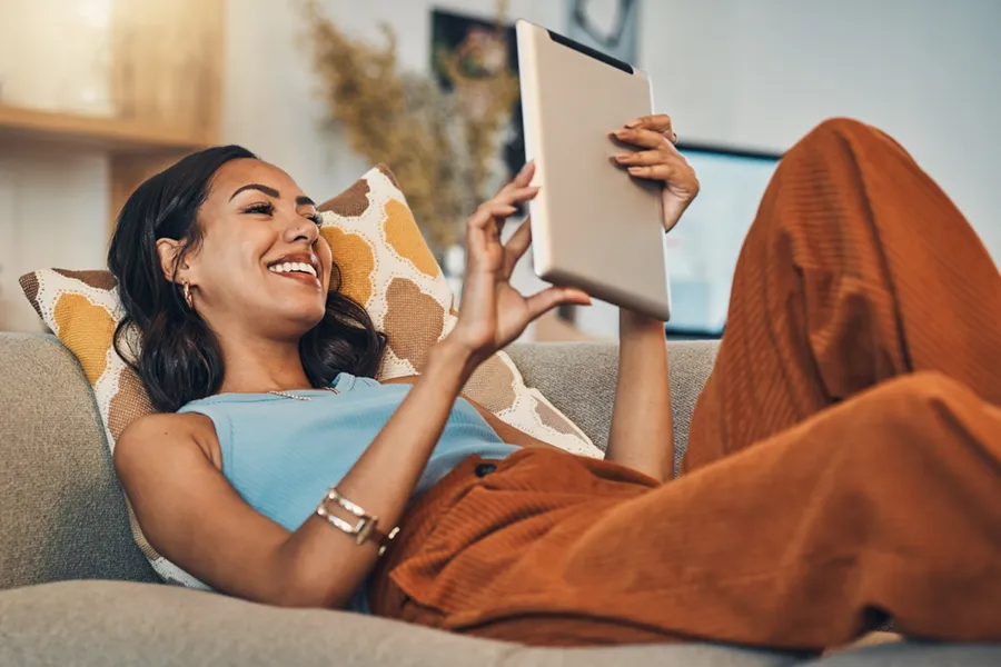 Middle-aged woman lounging on a couch with a tablet, enjoying her climate controlled home.