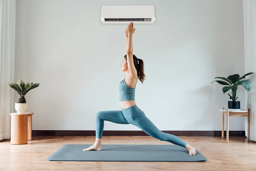 A young Asian woman performing yoga in her living room, under a ductless heat pump keeping her room climate-controlled.