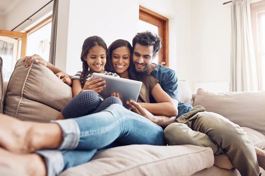 A young family sitting together on the couch, watching something on a tablet.